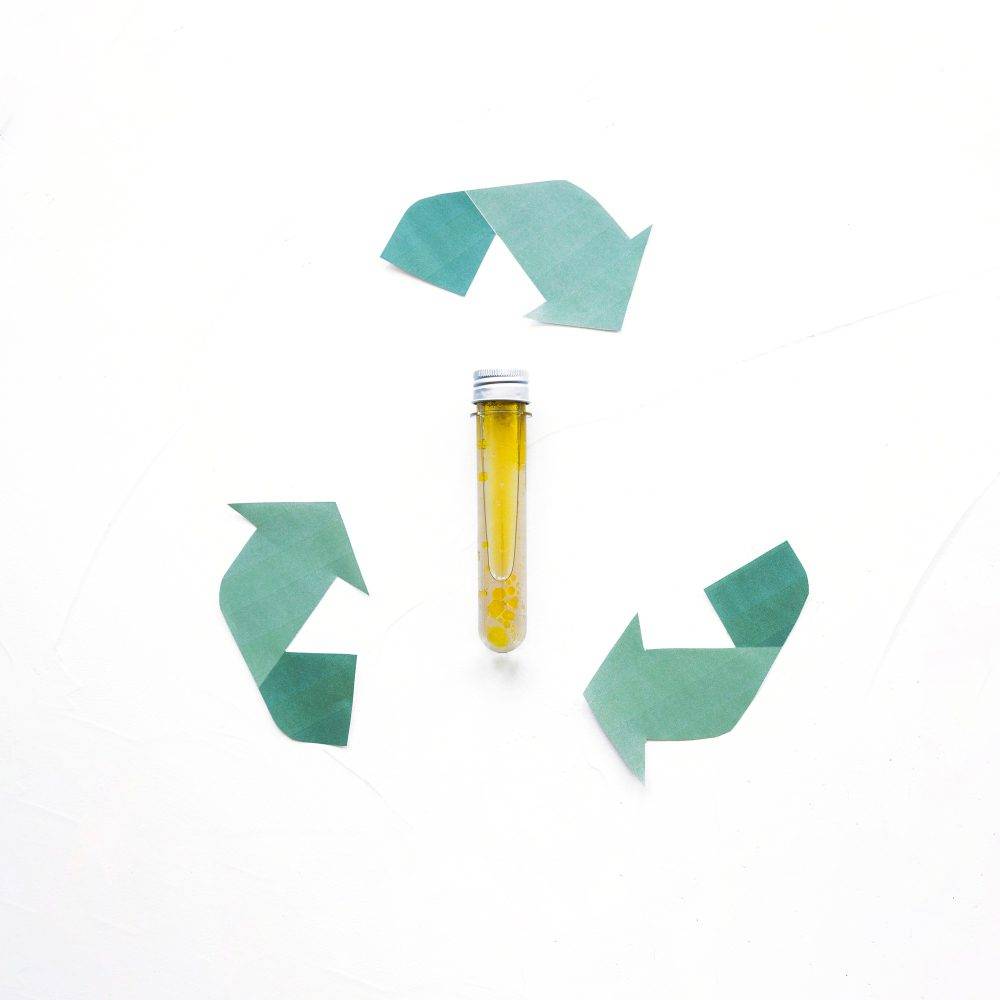 A test tube filled with used cooking oil surrounded by green recycling arrows, symbolizing eco-friendly used cooking oil management practices.