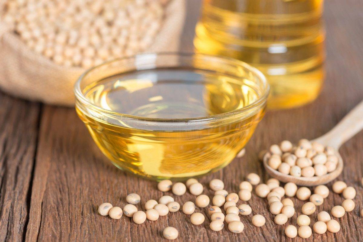 A clear bowl of golden soybean cooking oil, surrounded by soybeans on a rustic wooden table, showcasing the health benefits of soybean cooking oil.